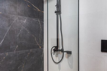 Halu! Modern bathroom with a sleek black shower fixture and elegant glass partition set against a marble wall creating a luxurious and contemporary showering space