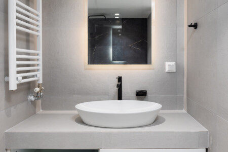 halu! Modern minimalist bathroom with a sleek gray countertop and white sink below an illuminated mirror offering a spacious feel and contemporary design appeal.