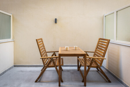 halu! A cozy patio setting with a wooden table and two matching chairs on a concrete floor ideal for outdoor relaxation or small gatherings in a serene atmosphere