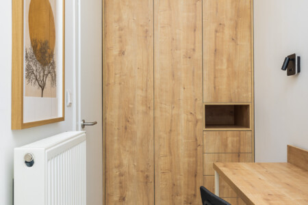 halu Cozy minimalist workspace with wooden desk and chair set against a tall wooden cabinet features wall art and a radiator creating a serene and functional home office environment