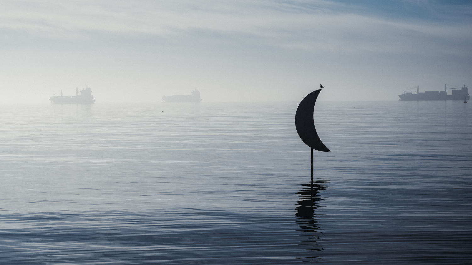 Half Moon sculpture standing in the sea at Thessaloniki waterfront with ships in the misty background.