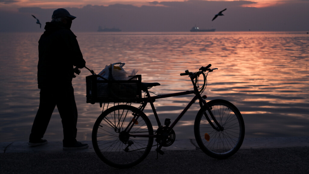 Silhouette of a fisherman with a bicycle by the sea at Nea Paralia, Thessaloniki during sunset.