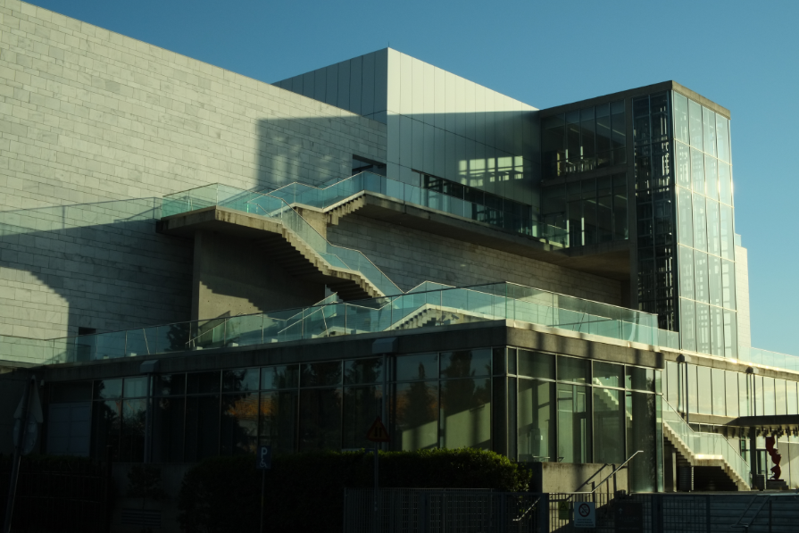Close-up of the modern white and glass M2 building of Megaro Mousikis Thessalonikis, featuring geometric lines, glass railings, and an external staircase in the sunlight.
