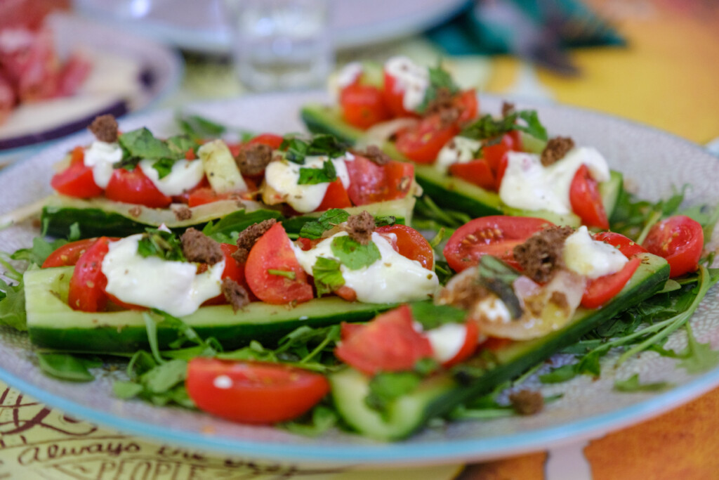 Fresh cucumber boats with cherry tomatoes, cheese, herbs, and croutons on a serving plate