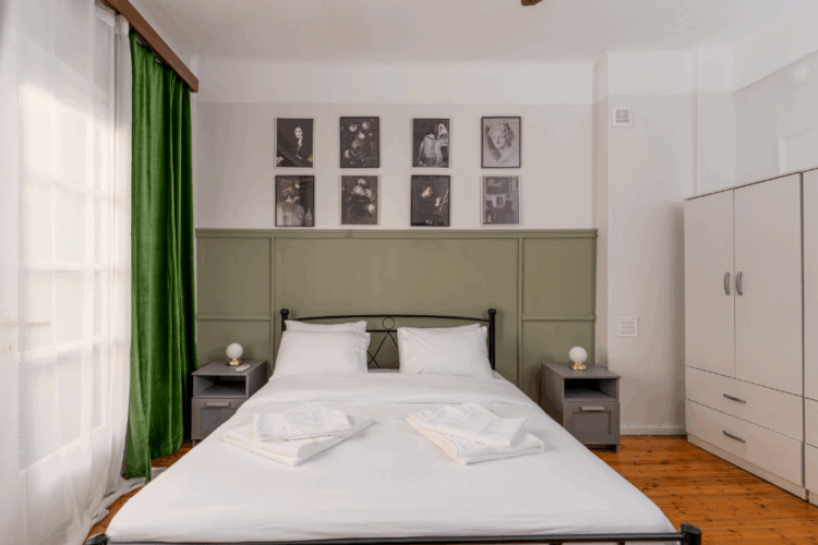 halu! Cozy bedroom with a modern design featuring a neatly made double bed, green curtains, and stylish wall art. Soft natural light creates a warm and inviting atmosphere.