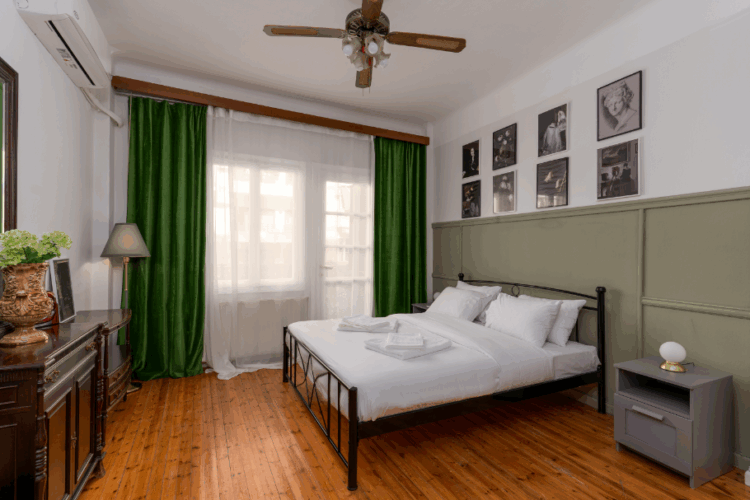 halu! Cozy bedroom featuring a double bed with white linens, wooden flooring, green curtains, wall art, and soft lighting for a comfortable and inviting atmosphere.