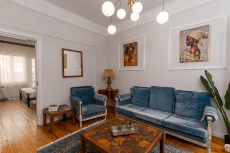 Halu! Spacious living room with blue velvet sofa and armchairs vintage wood flooring elegant artwork bright lighting and a cozy atmosphere for relaxation or gathering.