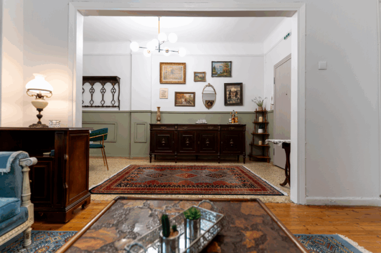 Halu! Cozy living room featuring vintage decor with a wooden floor ornate carpet elegant chandelier and art-adorned walls creating a warm inviting atmosphere