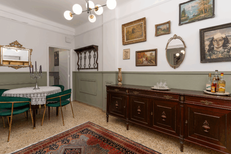 Halu! Cozy vintage dining room with elegant decor featuring a polished wooden buffet sideboard, a round dining table with green chairs, and framed artwork on the walls.