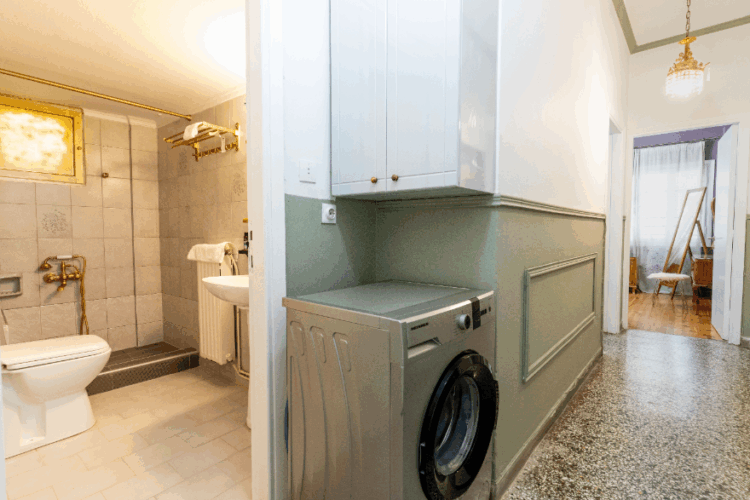 halu! Modern bathroom with tiled walls and a washing machine in an adjacent hallway. Features white cabinets and marble flooring for a sleek and clean design.