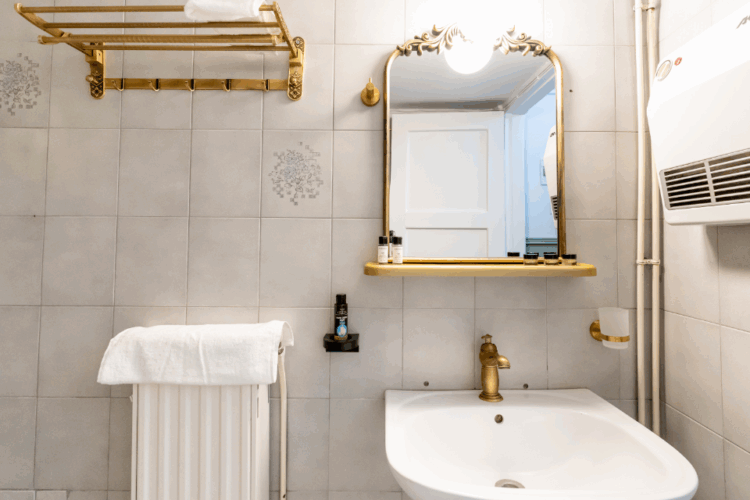 Halu! Elegant bathroom featuring a white ceramic sink with a sleek gold faucet and matching framed mirror offering a luxurious and stylish design complemented by a towel rack.