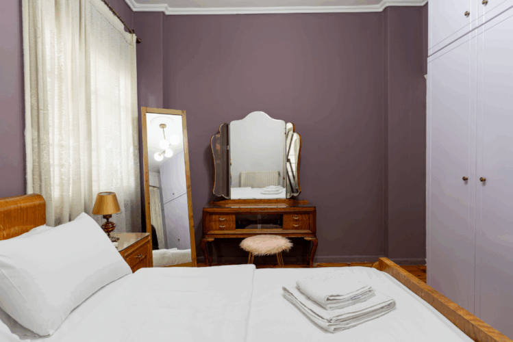 halu A cozy bedroom with a comfortable bed and fresh linens a vintage dressing table with a mirror and serene purple walls creating a relaxing ambiance