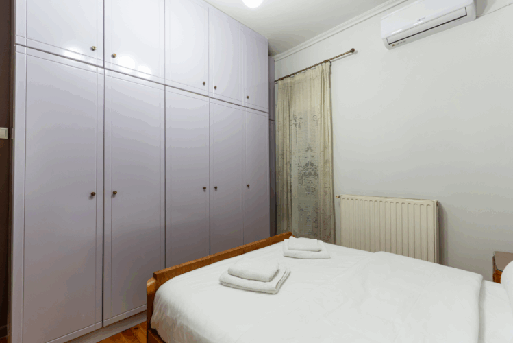 halu! Cozy bedroom with a comfortable bed neatly made with white linens and towels. Features purple built-in wardrobes and a wall-mounted air conditioning unit.