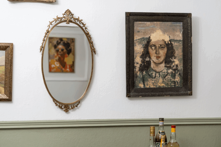Halu! Elegant wall featuring vintage paintings and an ornate mirror creating a classic artistic atmosphere with bottles visible on a shelf below for a cozy vibe.