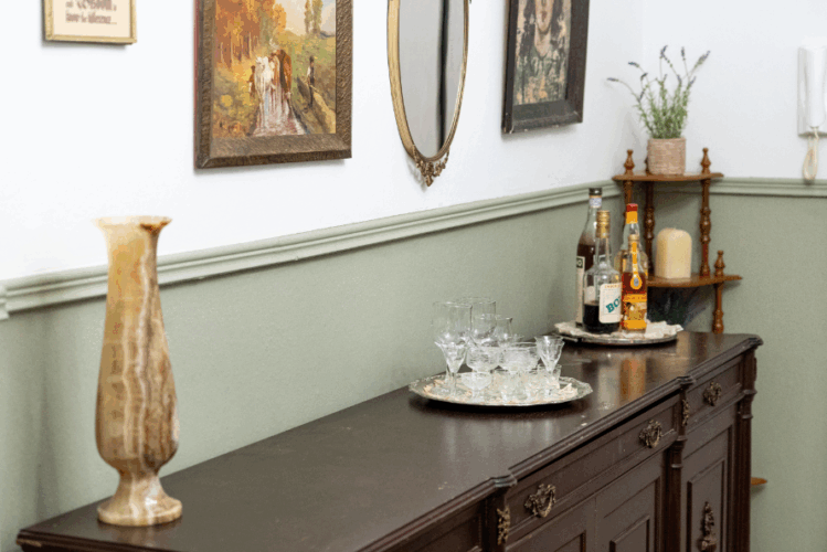 halu! Elegant dining room interior featuring a classic wooden sideboard adorned with vintage decor wine glasses bottles artwork and greenery creating a cozy ambiance