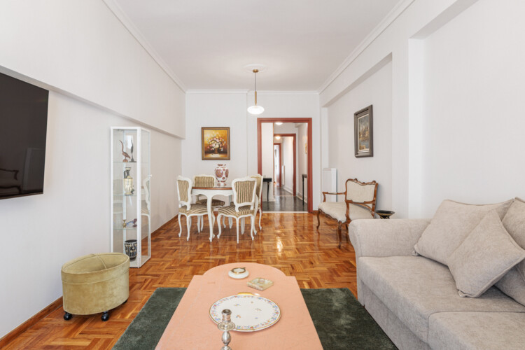 Elegant living room with classical décor, cozy sofa and armchairs, flat-screen TV, and a dining area. Large windows bring natural light, creating a bright and welcoming atmosphere.