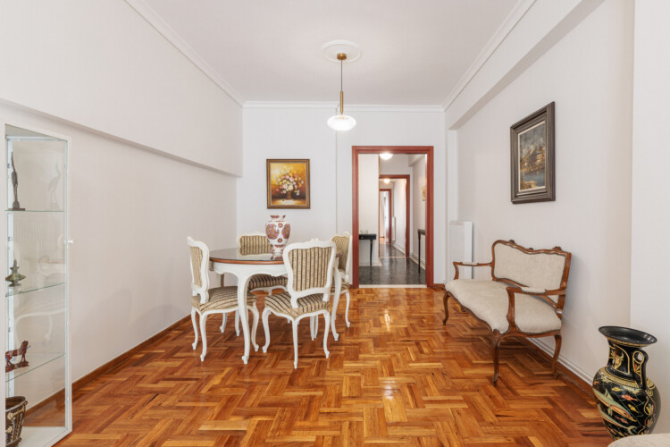 Elegant living room with classical décor, cozy sofa and armchairs, flat-screen TV, and a dining area. Large windows bring natural light, creating a bright and welcoming atmosphere.