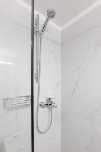 Modern bathroom with elegant marble-style tiles, a glass shower, fresh towels, and a washing machine. Bright and stylish, designed to offer both comfort and practicality during your stay.