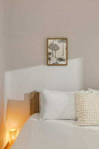 halu A cozy bedroom with a neatly made bed in white linens soft pillows and a framed picture of palm trees on the wall creating a relaxing and serene atmosphere