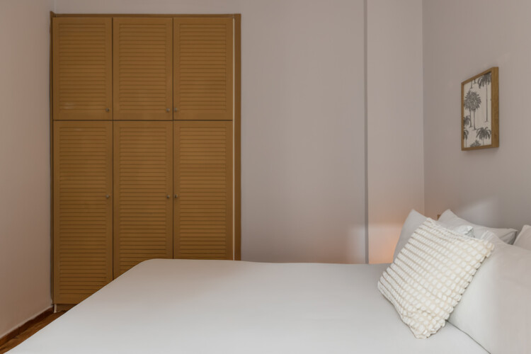 halu! Cozy bedroom featuring a comfortable bed with white linens and pillows a wooden wardrobe with louvered doors and a framed picture on a neutral wall creating a serene atmosphere