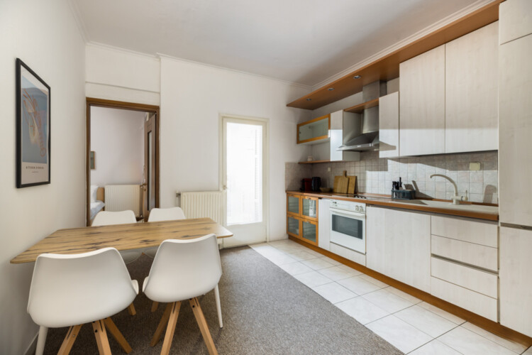 halu! Modern kitchen with white cabinetry and wooden accents. Includes dining table with chairs, built-in oven, stovetop, and sink. Bright and minimalist interior design.