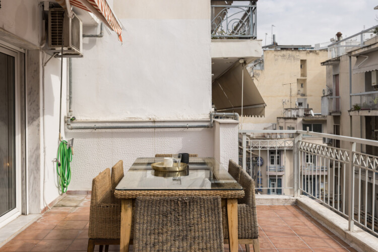 Halu! Cozy urban balcony with a wicker dining set overlooking neighboring buildings. Ideal for enjoying meals outdoors and experiencing city life from above.