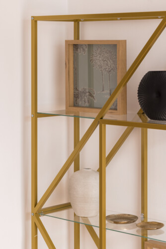 Halu! Modern gold metal shelf unit with glass shelves displaying decorative items including a framed artwork, black vase, and ceramic pot adding elegance to a room.