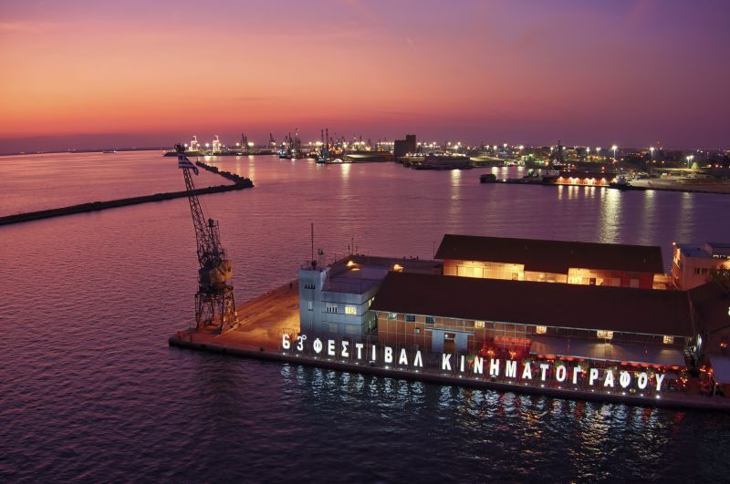 Halu! A vibrant sunset casts a warm glow over a waterfront film festival venue with illuminated signage creating a striking contrast against the colorful evening sky.