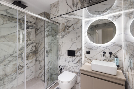 halu! Modern bathroom with marble walls featuring a sleek shower enclosure circular mirror floating vanity counter and a stylish contemporary design ambiance