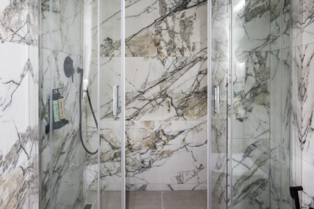 halu! Modern bathroom with marble walls featuring a sleek shower enclosure circular mirror floating vanity counter and a stylish contemporary design ambiance