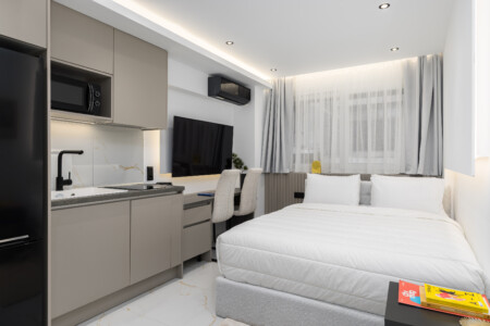 halu! Modern studio apartment interior featuring a cozy bed a fully equipped kitchenette a workspace with a chair flat screen TV and ambient lighting for comfort