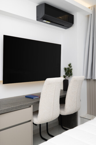 Halu! Modern minimalistic home office setup featuring a sleek desk with two soft chairs and a large flat-screen TV mounted on the wall. Stylish and inviting workspace.