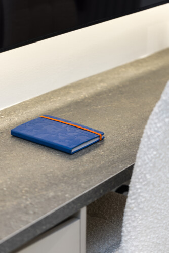 Halu! A blue notebook with an orange elastic band lies on a gray stone desk surface in a modern workspace setting offering a minimalist and organized aesthetic.