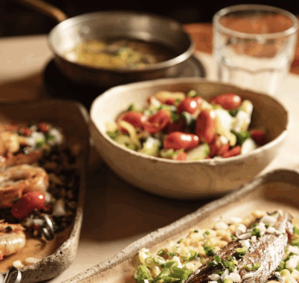 Halu! A table set with a vibrant Mediterranean meal featuring grilled shrimp, fresh salad with tomatoes and cucumbers, and a savory soup in a cozy dining atmosphere.