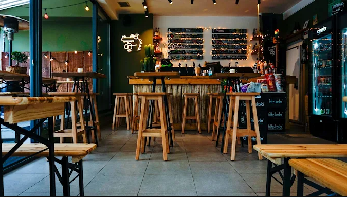 Halu! Cozy cafe interior with wooden tables and stools warm lighting and a view of the menu and drink selection creating a welcoming atmosphere for patrons