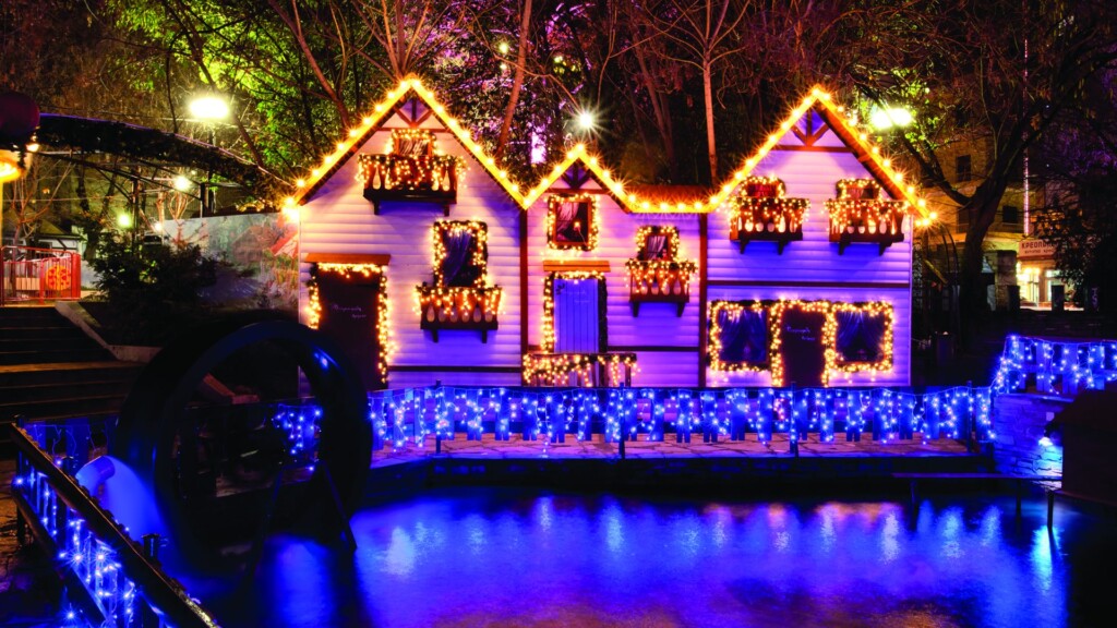 Halu! Festive Christmas village illuminated with colorful lights and decorations near a peaceful stream creating a magical holiday atmosphere and enchanting winter scene