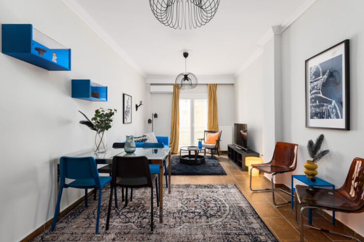 Halu! Modern living room with eclectic decor featuring vibrant chairs colorful accents and contemporary lighting. Large window provides natural light enhancing the cozy atmosphere.