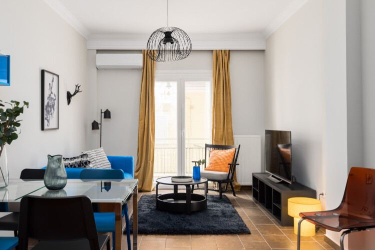 halu! A modern living room with stylish decor features a blue sofa, glass dining table, vibrant cushions, wall art and floor lamp creating a cozy and inviting atmosphere