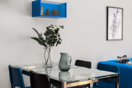 halu! Modern dining area with glass table and blue chairs elegant decor and art on the wall stylish interior design for a contemporary living space