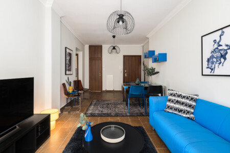 Halu! Modern living room with a blue sofa, stylish black decor, and a cozy seating area. Features wooden flooring, chic lighting, and contemporary artwork accents.