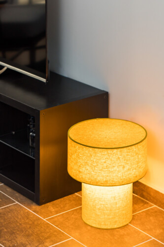 halu! Modern living room with a warm glowing lamp beside a black TV stand on a tiled floor creating a cozy ambiance in a stylish home interior setting.