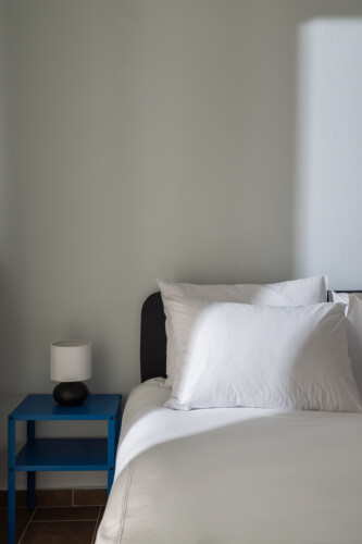 Halu! Cozy Indiana by halu! modern bedroom with plush white bedding and a sleek blue bedside table featuring a stylish lamp for a relaxing ambiance.