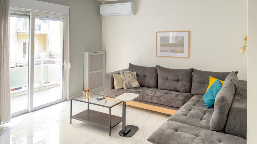 Halu! Bright modern living room featuring sleek gray sectional sofas yellow and teal accent pillows minimalist decor a framed art piece and sliding glass doors to balcony.