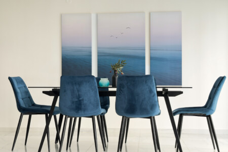 Halu! Modern dining room with a sleek table and six blue velvet chairs set against a minimalist backdrop adorned with soothing ocean-themed artwork.