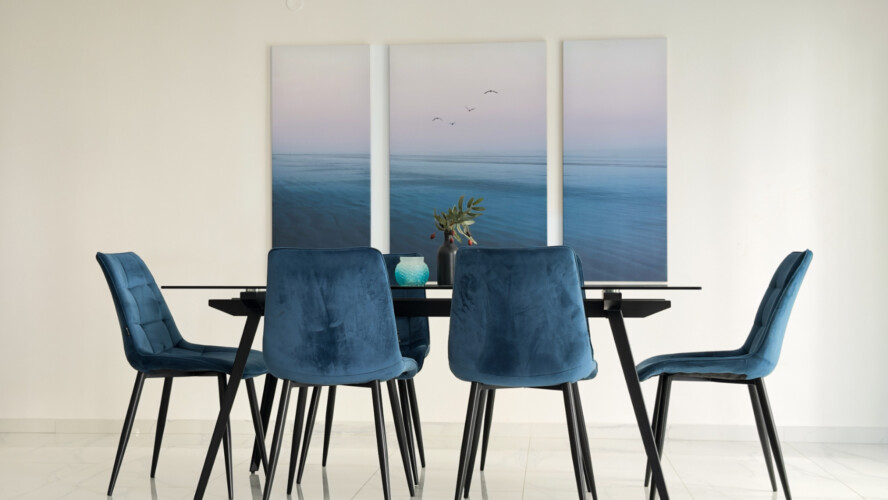 Halu! Modern dining room with a sleek table and six blue velvet chairs set against a minimalist backdrop adorned with soothing ocean-themed artwork.
