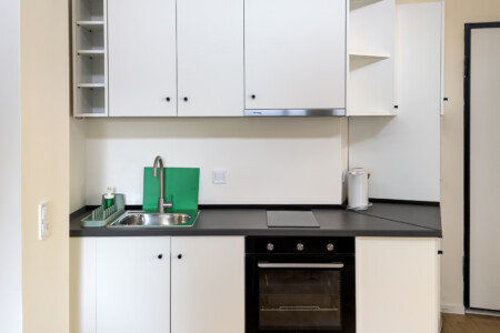 halu! Modern kitchenette featuring sleek white cabinets minimalist design black countertop stainless steel sink integrated oven ideal for compact practical living spaces