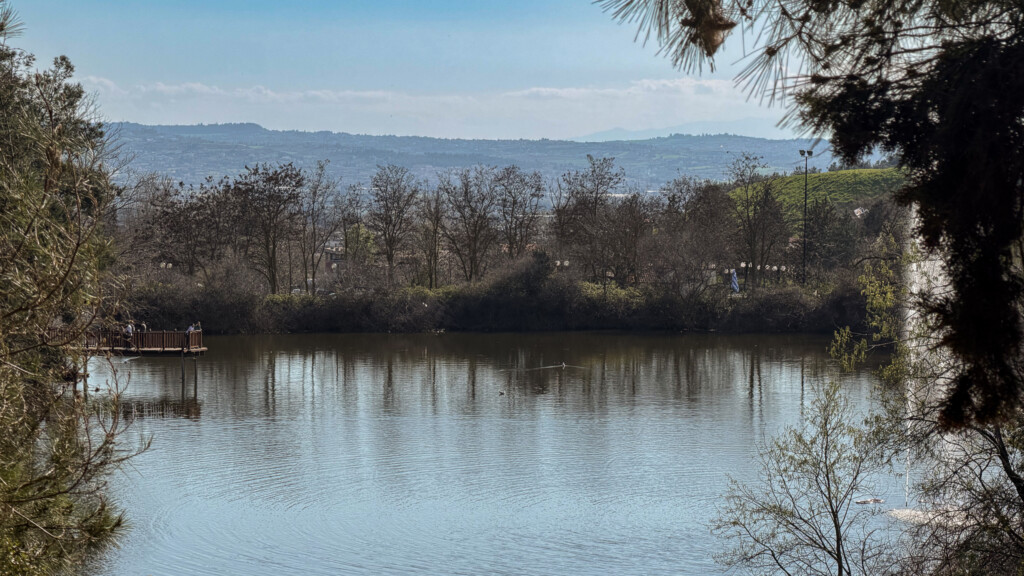 Halu! Discover the tranquil beauty of Thermi Dam in Thessaloniki. This green escape offers a serene view of the water surrounded by lush trees and clear skies.