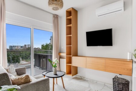 Halu! Modern living room with large window view stylish furniture wall-mounted TV wooden shelving cozy decor indoor plant and ambient lighting creating a relaxing space.