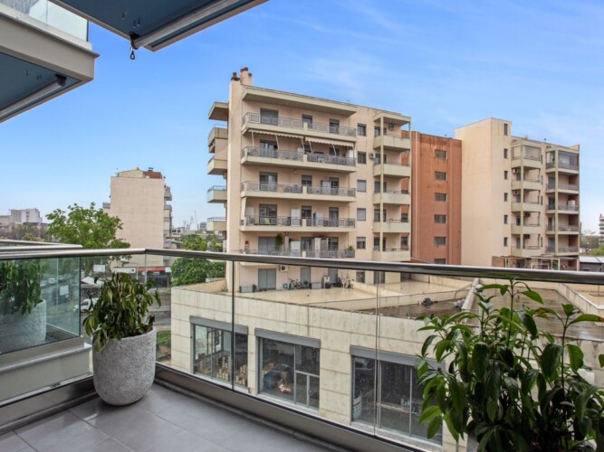 Halu! A modern balcony view featuring urban residential buildings under a clear blue sky. Green plants add a touch of nature to the sleek design of the space.