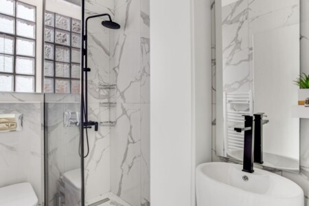 Halu! Elegant modern bathroom featuring marble tiles a sleek black shower fixture and a stylish basin. Bright natural light enhances the clean and minimalist design.